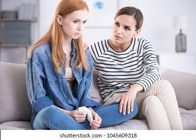 Woman comforting an emotional young teenage girl sitting with her legs crossed on a sofa and crying