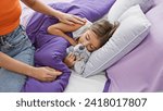 A woman comforts a sleeping girl with a stuffed animal in a cozy bedroom, depicting a tender family moment.