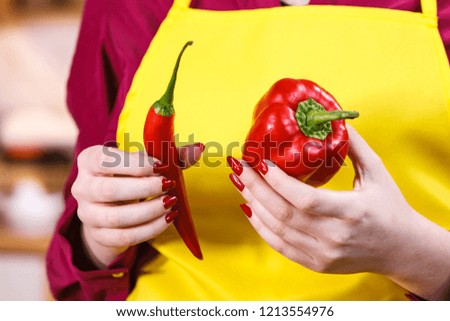Woman comparing bell pepper and red hot chilli. Vegetables, spices, food concept.