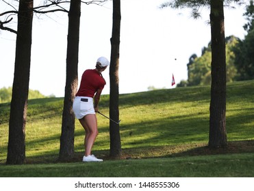 A woman competing in a golf tournament, hits a shot between trees.