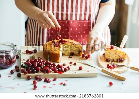 Woman confectioner in an apron decorating a cherry cake with cherries, a Homemade birthday cake. Summer fruit cake, vegan dessert, Selective focus.