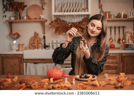Woman confectioner decorates candy in the form of black skulls for Halloween with gold. The process of creating candies for Halloween