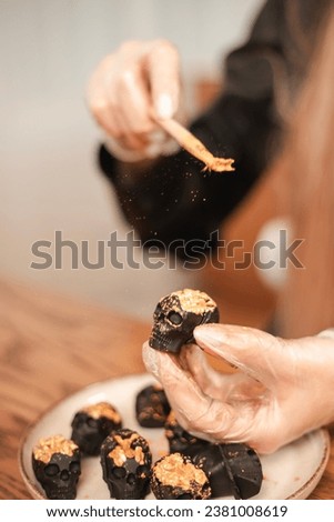 Woman confectioner decorates candy in the form of black skulls for Halloween with gold. The process of creating candies for Halloween