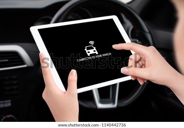 Woman connecting car with her tablet and\
app using wifi, steering wheel in\
background
