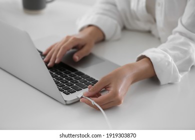 Woman connecting charger cable to laptop at white table, closeup