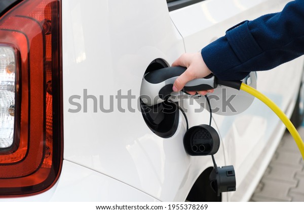 Woman connecting power supply to electric\
vehicle for charging.