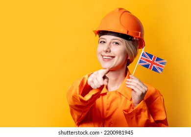 Woman Construction Worker In Helmet And Orange Overalls Holding GB Flag Against A Yellow Background