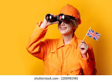 Woman Construction Worker In Helmet And Orange Overalls With Binoculars And GB Flag On Yellow Background