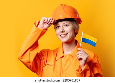 Woman Construction Worker In Helmet And Orange Overalls Holding Ukrainian Flag Against A Yellow Background 