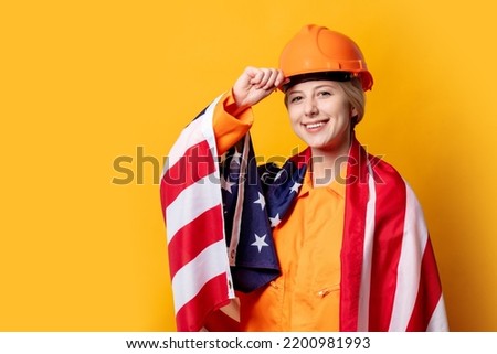 woman construction worker in helmet and orange overalls with USA flag against a yellow background 