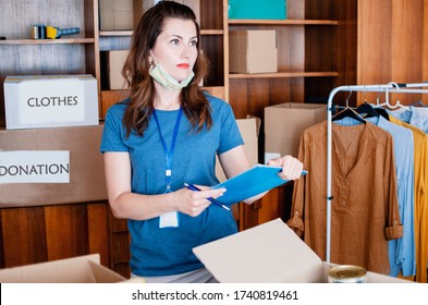 Woman Controller In Charitable Foundation Take Care Of Packing Donation Box With Humanitarian Aid.Delivery Employee In Blue T-shirt Uniform Face Mask And Empty Cardboard Box 