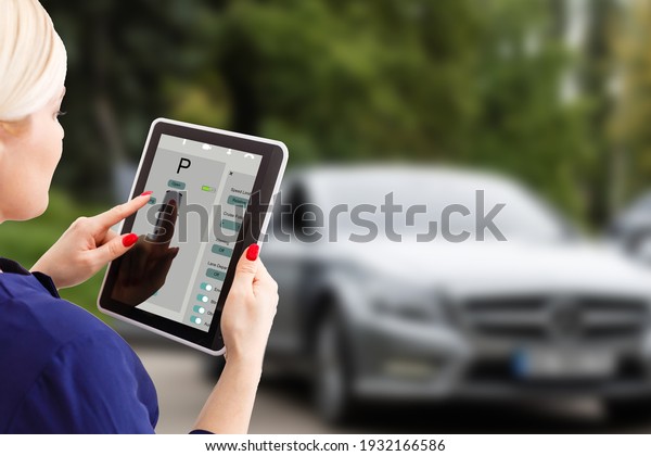 Woman controlling car with tablet application
while standing near the vehicle outdoors, close-up view on the
tablet with app interface