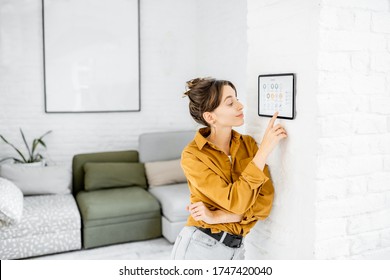 Woman Controlling Home With A Digital Touch Screen Panel Installed On The Wall In The Living Room