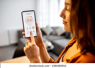 Woman controlling home heating temperature with a smart home, close-up on phone. Concept of a smart home and mobile application for managing smart devices at home - Shutterstock ID 1584383965