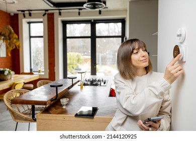 Woman controlling home temperature with electronic thermostat mounted on the wall in living room at home. Concept of modern technologies and smart home