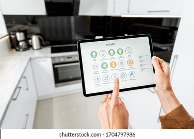Woman controlling kitchen appliances with a digital tablet, close-up on mobile device with launched smart home application. Smart home concept