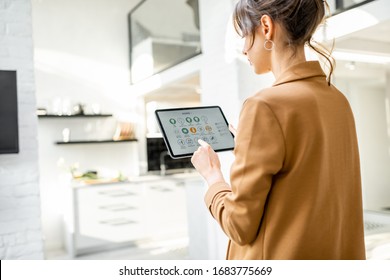 Woman controlling smart home devices using a digital tablet with launched application in the white living room. Smart home concept