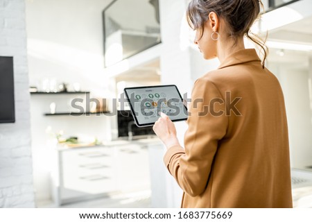 Woman controlling smart home devices using a digital tablet with launched application in the white living room. Smart home concept