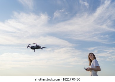 A Woman Controls The Flight Of A Drone. The Quadcopter Hovered In The Air, The Female Drone Pilot Looks At The Drone