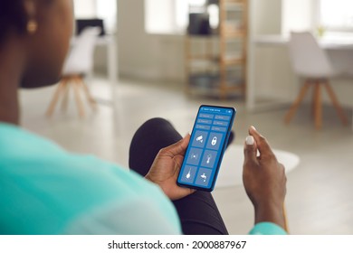 Woman controls Smart Home on cellphone. Close up African American lady holding cell phone using mobile interface with door lock, faucet etc icons to monitor house system. People and technology concept