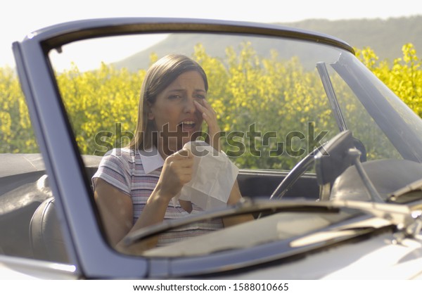 Woman in\
convertible rubbing eye and holding\
tissue