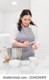 A Woman Cook Breaks An Egg With A Knife To Prepare Cream Or Dough In A Mixer Bowl. Cooking Courses And Dessert Recipes. Family Business. Online Lessons For Cooks.