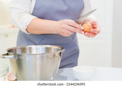 A Woman Cook Breaks An Egg With A Knife To Prepare Cream Or Dough In A Mixer Bowl. Cooking Courses And Dessert Recipes. Family Business. Online Lessons For Cooks.