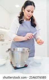 A Woman Cook Breaks An Egg With A Knife To Prepare Cream Or Dough In A Mixer Bowl. Cooking Courses And Dessert Recipes. Family Business. Online Lessons For Cooks.