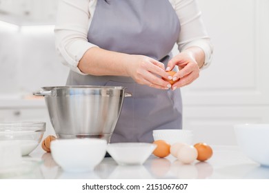 A Woman Cook Breaks An Egg To Prepare Cream Or Dough In A Mixer Bowl. Cooking Courses And Dessert Recipes. Family Business. Online Lessons For Cooks.