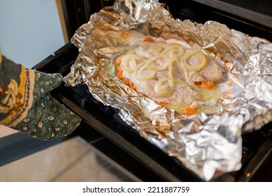 A Woman Cook Takes Out A Dish Of Baked Fish From The Oven