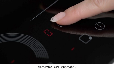 A Woman Cook Turns On An Electric Induction Cooker. Housewife Prepares Food On Stove. Touch Black Glass-ceramic Panel. Switching On The Burner Cooktop.