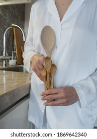 A Woman Cook In A White Uniform On The Background Of The Kitchen Is Holding Wooden Spoons Of Different Sizes And Is Going To Cook Dinner. Wooden Spoons Close Up