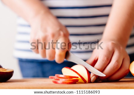 Woman cooking and cutting apple on wooden cutting board. Preparing healthy food. Hands holding knife and slicing fruits on table in kitchen