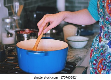 Woman Is Cooking Dinner In A Blue Cast Iron Pot, Dutch Oven, On A Stove