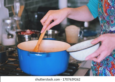 Woman Is Cooking Dinner In A Blue Cast Iron Pot, Dutch Oven, On A Stove