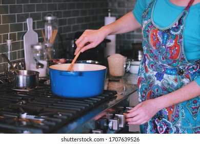 Woman Is Cooking Dinner In A Blue Cast Iron Pot, Dutch Oven, On A Stove