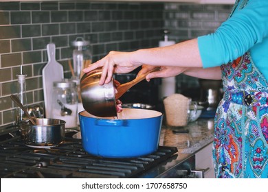 Woman Is Cooking Dinner In A Blue Cast Iron Pot, Dutch Oven, On A Stove