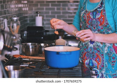 Woman Is Cooking Dinner In A Blue Cast Iron Pot, Dutch Oven, On A Stove