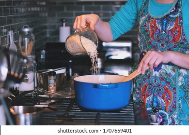 Woman Is Cooking Dinner In A Blue Cast Iron Pot, Dutch Oven, On A Stove