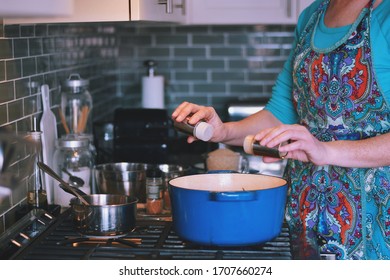 Woman Is Cooking Dinner In A Blue Cast Iron Pot, Dutch Oven, On A Stove