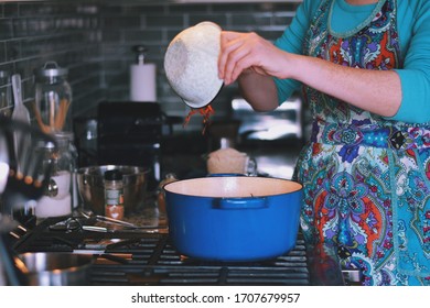 Woman Is Cooking Dinner In A Blue Cast Iron Pot, Dutch Oven, On A Stove