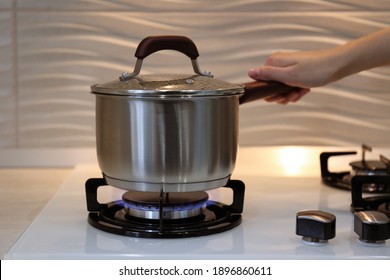 Woman cooking food in pot on modern kitchen stove with burning gas indoors, closeup