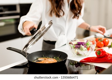 Woman Cooking Fresh Fish Steak On The Kitchen With Vegetables And Glass Of White Wine And Spices. Housewife Concept