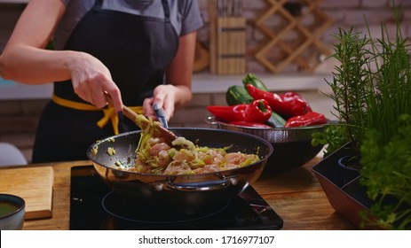 Woman Cooking Frying Chicken Meat In Wok Pan On Kitchen Table. Closeup Hands. Cosy Dark Room. Real, Authentic Cooking.