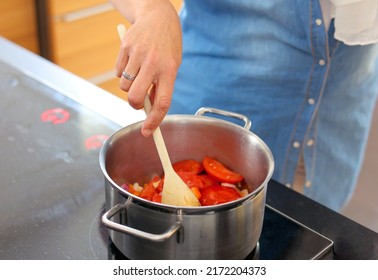 A Woman Cooking Italian Cuisine, Making Tomato Soup Or Sauce For Pasta, Detailed View Of Hands Holding Wooden Spoon Stir Fried Chopped Tomatoes In A Pot On Electric Stove, Background For Text.