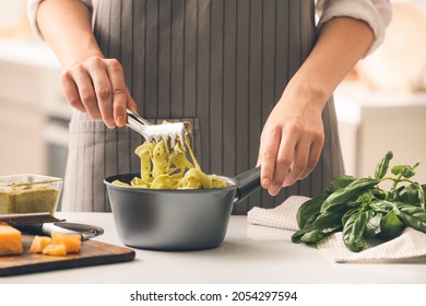 Woman Cooking Pasta With Pesto Sauce In Kitchen