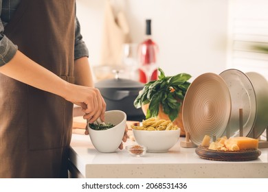 Woman Cooking Pasta With Pesto Sauce In Kitchen