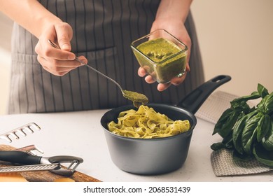 Woman Cooking Pasta With Pesto Sauce In Kitchen