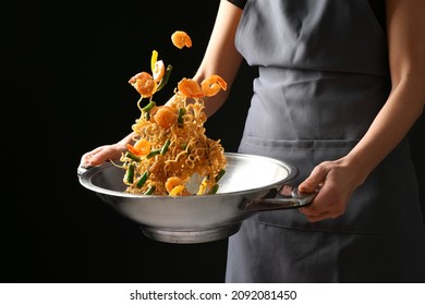 Woman cooking tasty Chinese noodles in wok on dark background