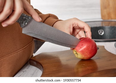 A woman cooks and slices an apple on a wooden chopping board. Cooking healthy food. Hands holding a knife and slicing fruit on the table in the kitchen. A woman in the kitchen cuts fruit into slices - Powered by Shutterstock